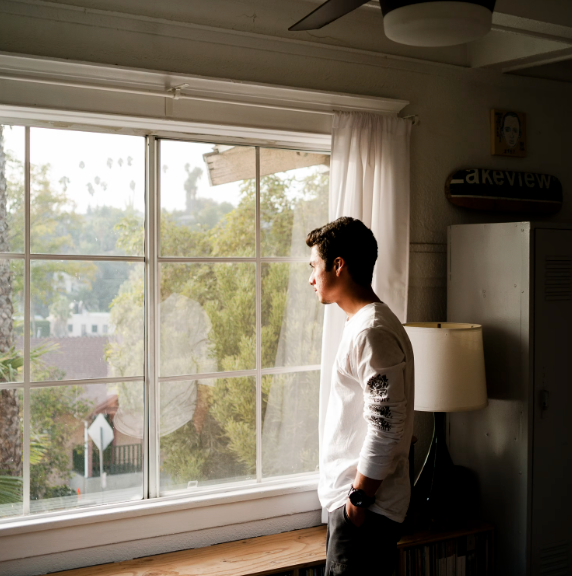 A person looking out of their living room window while waiting for someone to arrive